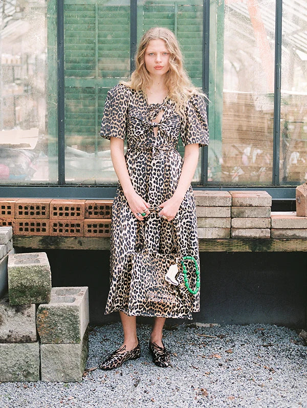 Model in a leopard print dress posing near a window, showcasing a trendy fashion look with a nature backdrop.